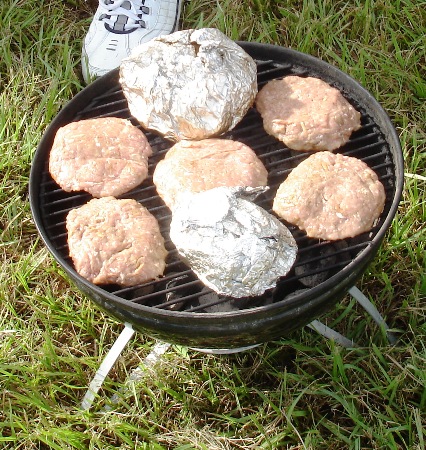 Burgers and baked potatoes on the grill at a tailgate party.